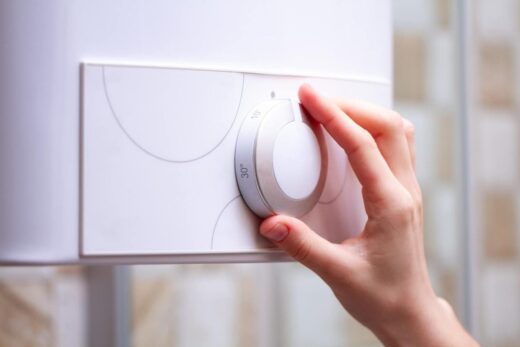 Main réglant le thermostat d'un appareil de chauffage mural