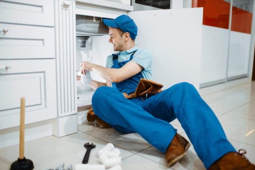 Plombier travaillant sous un meuble de cuisine